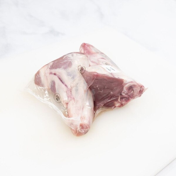 A pair of raw Welsh lamb hindshanks in a vacuum sealed pack on a white and gray marble background.