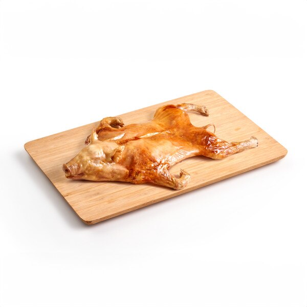 A whole, roasted suckling pig splayed stomach-side down across a wooden cutting board.