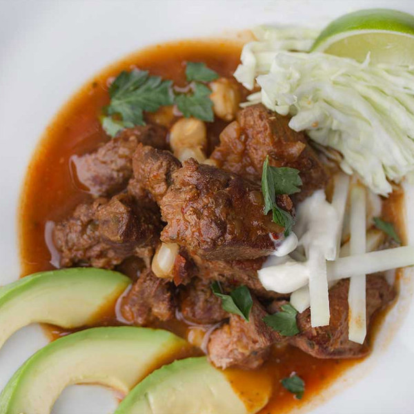 Posole with cooked wild boar meat, hominy, avocado, kohlrabi, cabbage, lime, red broth, white bowl