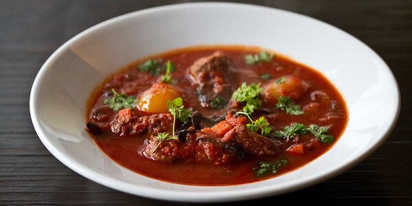 Elk stew, tomato broth, pearl onions, chervil sprigs, white bowl, black background