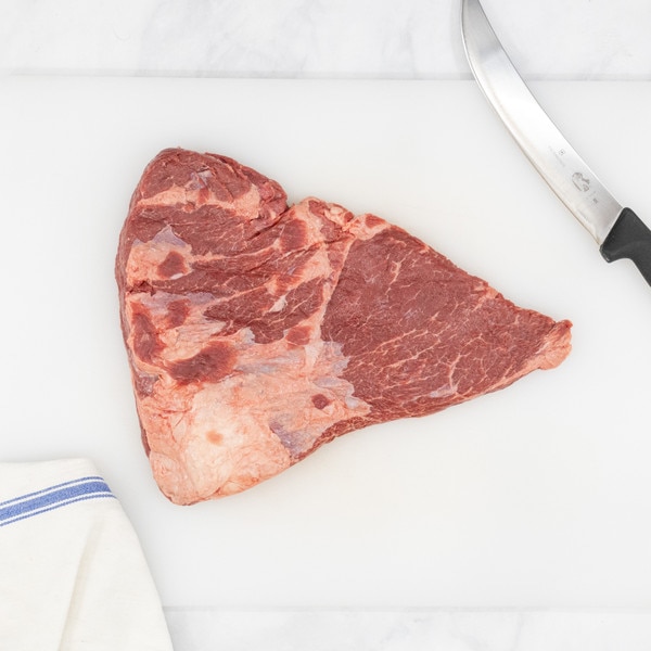 A raw Ocean Beef chuck rib on a white cutting board flanked by a blue-striped, white towel on the left and a chef’s knife on the right.