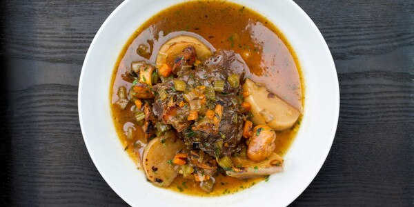 Grain-fed veal cheek stew with carrots, celery, chanterelle mushrooms & baby turnips, white bowl, black-stained wood background