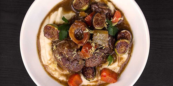 Grain-fed veal osso bucco braised with preserved lemon, figs, parsnip puree, white bowl, black background