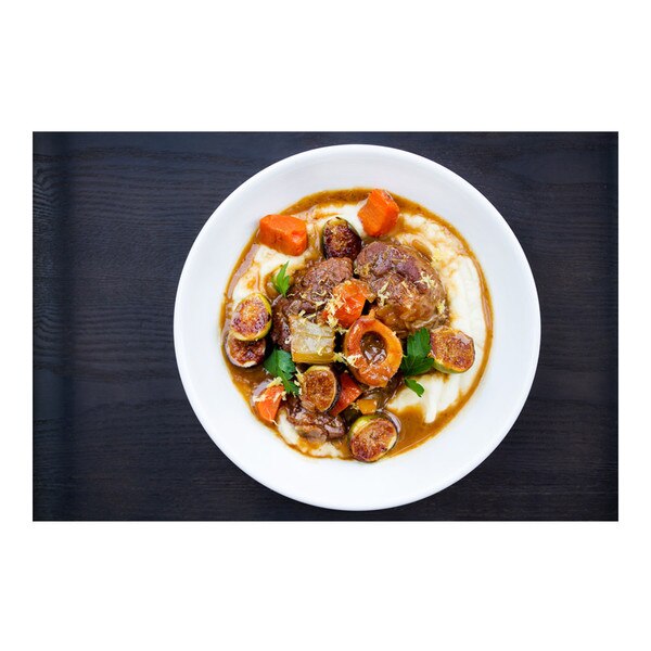 Grain-fed veal osso bucco braised with preserved lemon, figs, parsnip puree, white bowl, black background