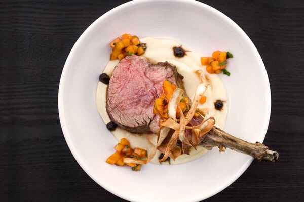 Cooked grain-fed veal rib chop, frenched bone, persimmon salad, fried parsnips, parsnip puree, black garlic puree, white plate, black background