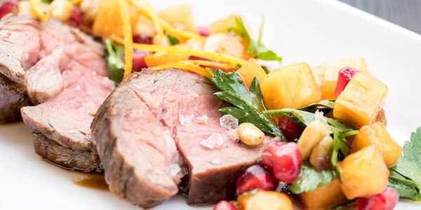 Cooked, sliced grain-fed veal tenderloin, persimmon, pomegranate, parsley, orange zest, pine nuts, salt flakes, white plate