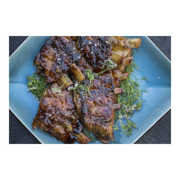 Cooked, glazed Iberico pork baby back ribs with flowering green herbs on blue plate