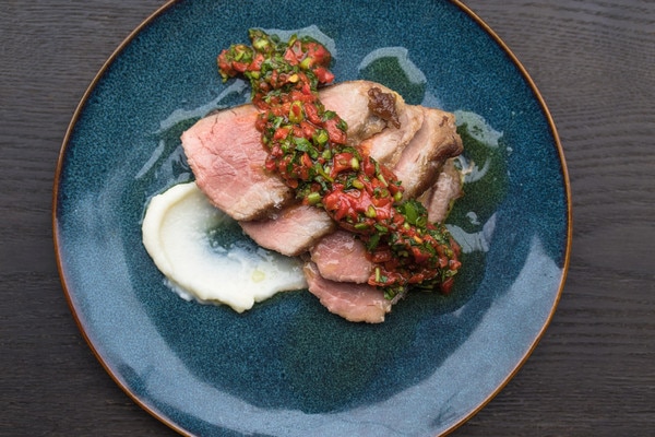 Slices of cooked acorn fed Iberico pork shoulder (presa), red pepper & parsley relish, white garlic sauce on blue plate