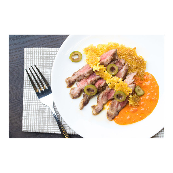 Cooked slices of Iberico pork end loin (pluma), yellow rice, sliced olives, red pepper sauce, white plate with napkin & fork