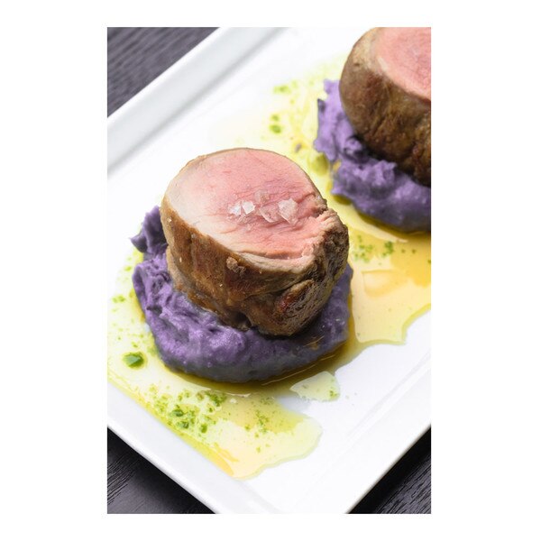 Cooked medallions of Iberico pork tenderloin with purple potato puree & parsley oil on a white plate