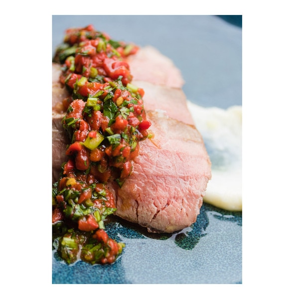 Slices of cooked Iberico pork shoulder (presa), red pepper & parsley relish, white garlic sauce on blue plate