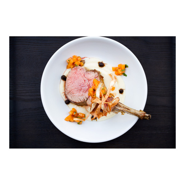 Cooked grain-fed veal rib chop, frenched bone, persimmon salad, fried parsnips, parsnip puree, black garlic puree, white plate, black background