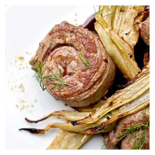 Cooked, spiral-rolled grass-fed lamb tenderloin with grilled fennel, fennel fronds & fennel pollen on white plate