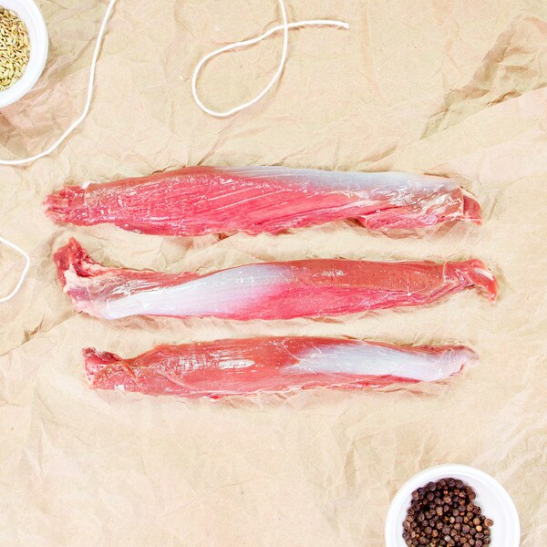 3 raw grass-fed lamb tenderloins horizontally on brown butcher paper, bowl of peppercorns, string