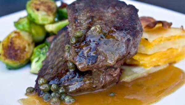 Cooked ostrich fan fillet medallions, capers, brown sauce, brussels sprouts, stacked potato gratin, white plate