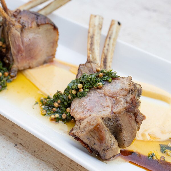 Green chimichurri with coriander seeds draped over cooked, double-bone petite veal chops on a white plate sauced with yellow lemon-caper cream, pureed white potato, and brown demi-glace