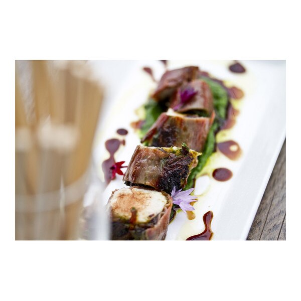 5 pieces of prosciutto-wrapped rabbit striploin atop green wild ramp puree, balsamic vinegar drizzle on white plate