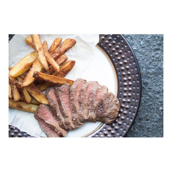 cooked, sliced flat iron steak next to fried potatoes on a white plate with a black rim