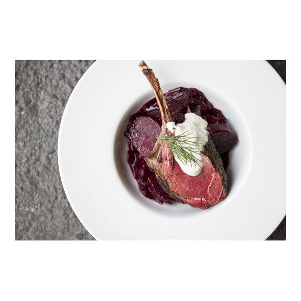 Sliced red beets in a white bowl with a cooked venison chop, a spoonful of horseradish cream and a sprig of fresh dill on top