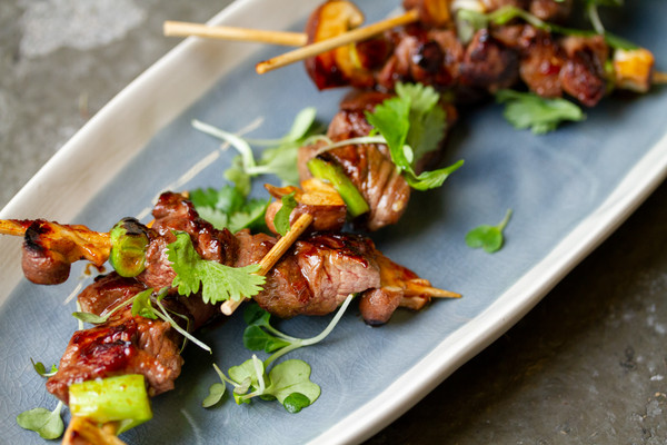 Cooked skewers of venison trim meat, cilantro leaves, oval blue-and-white plate, gray concrete background