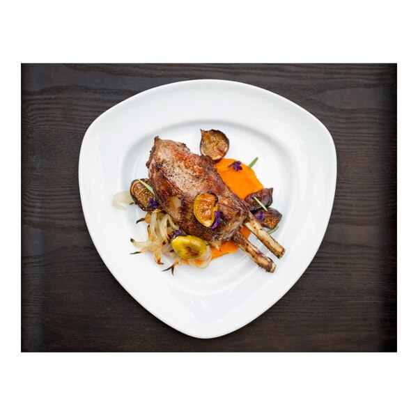 Cooked double-rib wild boar chop, sweet potato puree, grilled figs & onions, white triangular plate, black-stained wood background