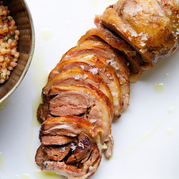 Cooked, stuffed, boneless grass-fed lamb shoulder, sliced, with a bowl of pearl couscous on a white background