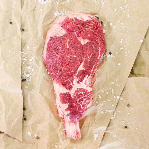 raw bone-in grass-fed beef cowboy ribeye steak, salt, butcher paper