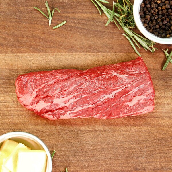 New Zealand grass-fed Angus beef hanger steak on a wooden board surrounded rosemary sprigs, a bowl of peppercorns & a bowl of butter