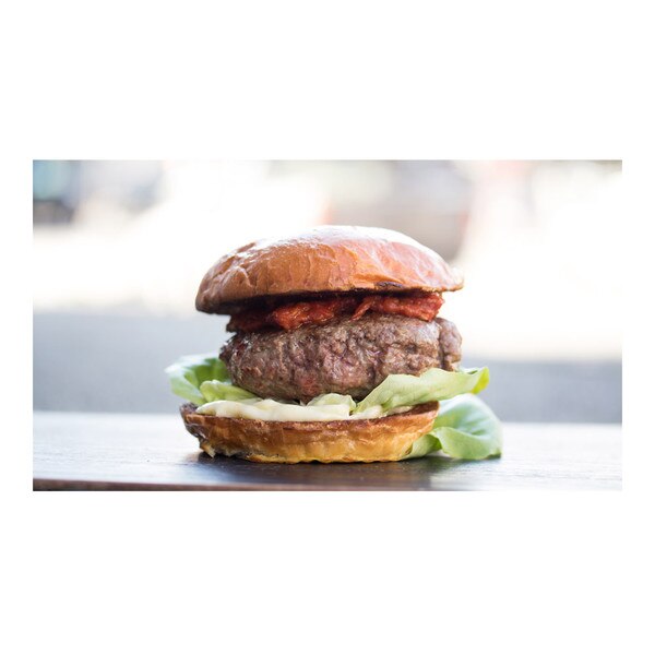 Cooked grass-fed lamb burger on a bun with lettuce, mayo, tomato jam, blurred background