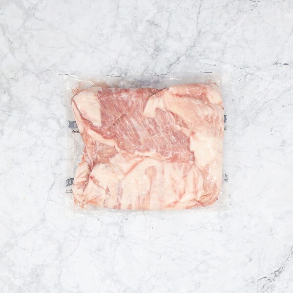 One package of raw Iberico pork belly filet, vacuum-sealed in clear plastic, against a gray-streaked white marble background.