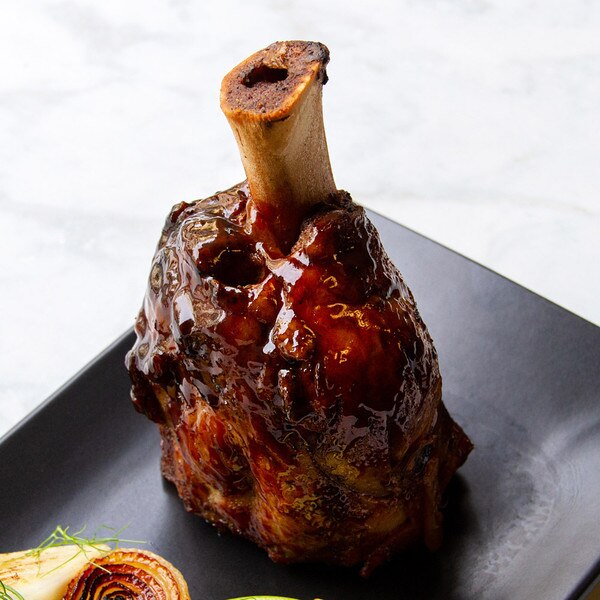 Cooked, glazed, Kurobuta pork hindshank on rectangular black plate with grilled onions