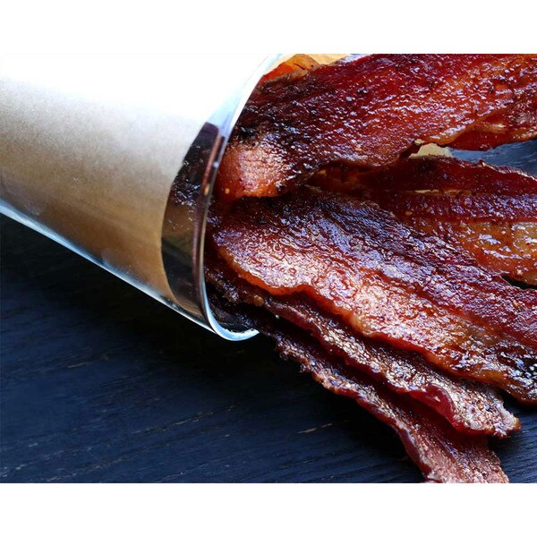 Cooked slices of Kurobuta bacon poking from a paper-lined cup on its side