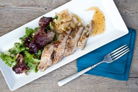 Cooked, sliced boneless Kurobuta loin pork chop, lettuce, grilled onions, plum sauce, rectangular white plate, blue napkin, fork