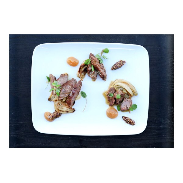 Cooked, sliced Kurobuta pork cheeks with roasted fennel, brown sauce & green herbs on white rectangular plate