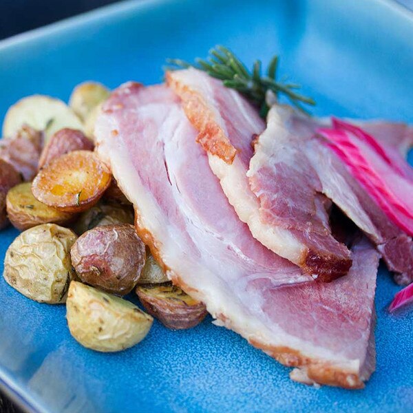 Slices of Kurobuta ham, roasted potatoes, sliced red onion, rosemary sprig on blue plate