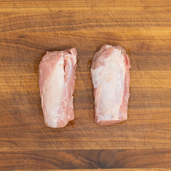 Two, raw, milk-fed French veal butt tenderloins on a wooden cutting board.