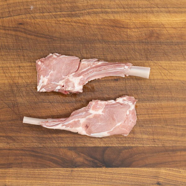 Two raw, milk-fed French veal chops for Milanese on a wooden cutting board.
