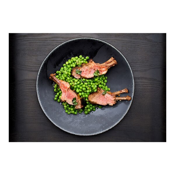 3 double-rib lamb chops with peas & herbs in a round black bowl on black-stained wood background