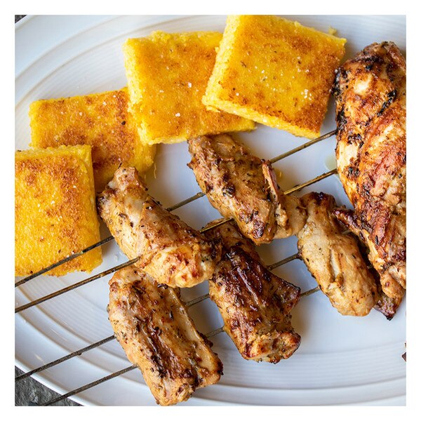 4 skewers holding 6 pieces of rabbit saddles & hind legs, yellow polenta squares, white oval plate