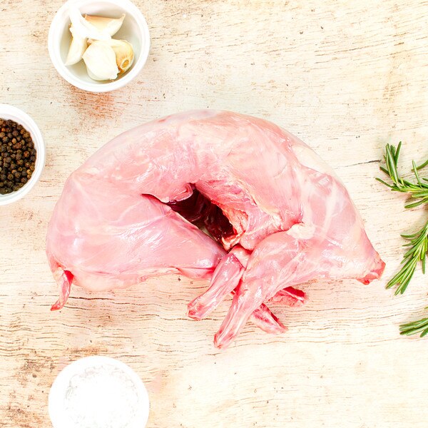 Whole, raw rabbit fryer, rosemary sprigs, bowls of salt & pepper, on whitewashed wood background