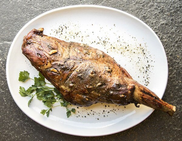 Cooked wild boar bone-in leg, salt, pepper, garlic, parsley, white plate on gray concrete background