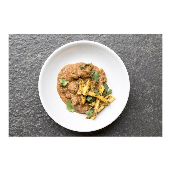 Wild boar boneless neck in masala curry sauce, sliced green mango pickle, parsley, white bowl, gray concrete background